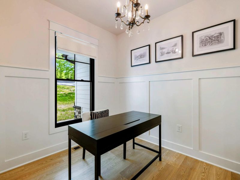 Office - Black desk with board-and-batten wainscoting, a crystal chandelier, and architectural prints on the wall.