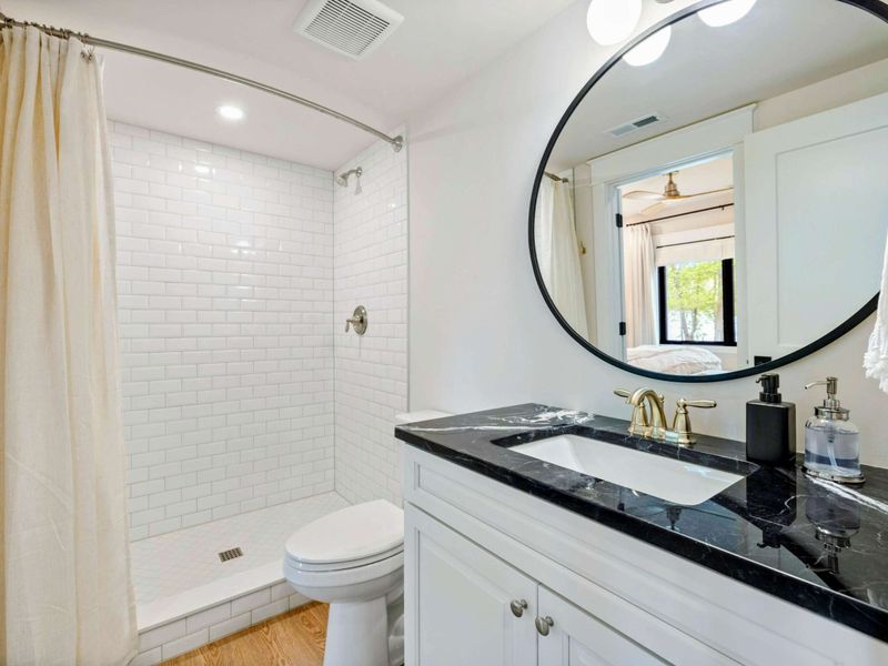Bathroom - White subway tile shower/tub combo, black marble vanity with a round mirror, and gold fixtures.