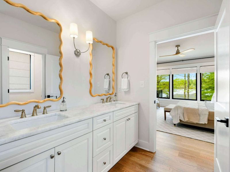 Spa-Like Simplicity – A spacious en-suite with double vanities, designer touches, and a window-framed view of the lake beyond.