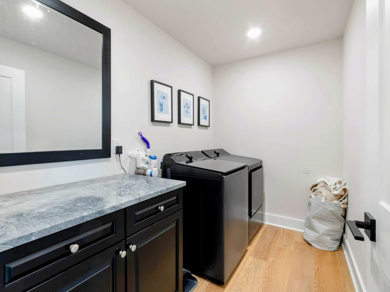 Laundry Room - Black washer and dryer with a dark cabinet, marble countertop, and framed blue prints on the wall.