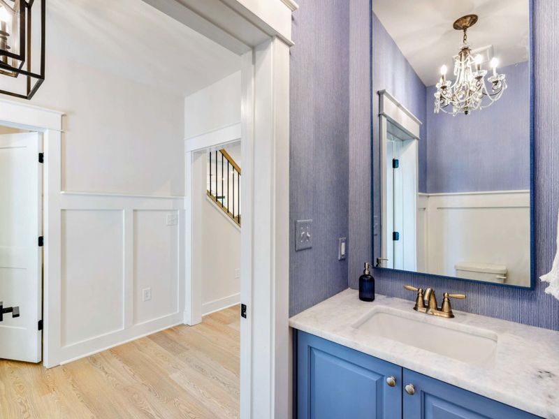 Powder Room - Periwinkle blue wallpaper and a matching blue vanity with marble top, crystal chandelier, and brass fixtures.