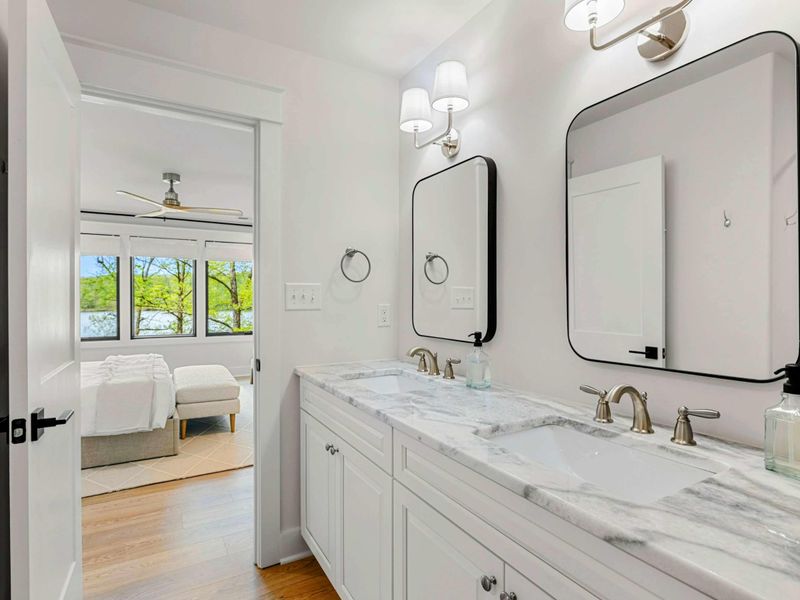 Primary Bathroom - Double vanity with marble top, black-framed mirrors, and brass fixtures, with a view through to the bedroom.