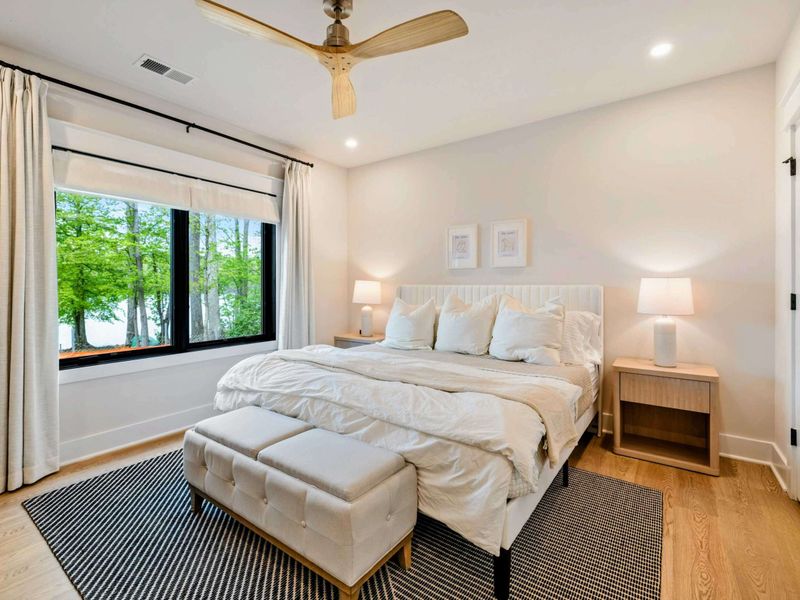 Bedroom 3 - King bed with a white headboard, tufted ottomans, and a herringbone area rug, with tree-filtered lake views.