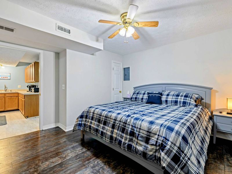 Bedroom - King bed with gray frame and plaid bedding, a view into the kitchenette area, and a mini-split AC unit.
