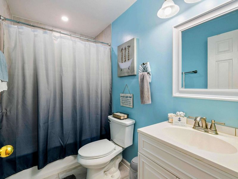 Bathroom - Bright sky-blue walls with a white vanity, ombre shower curtain, anchor decor, and coastal wall art.