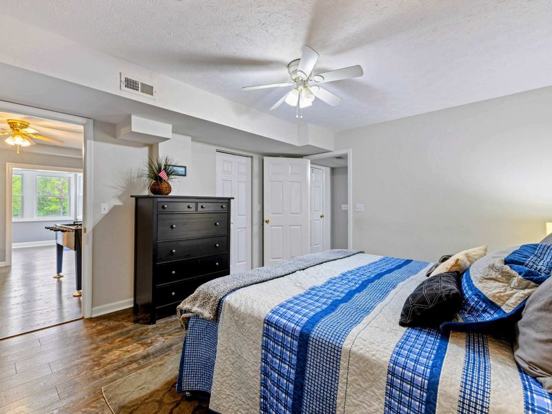 Bedroom - Queen bed with blue plaid bedding, black dresser, ceiling fan, and a view through to the adjacent bedroom.