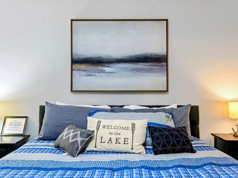 Bedroom - Closeup of the queen bed with a serene lake landscape painting and cozy "Welcome to the Lake" accent pillow.