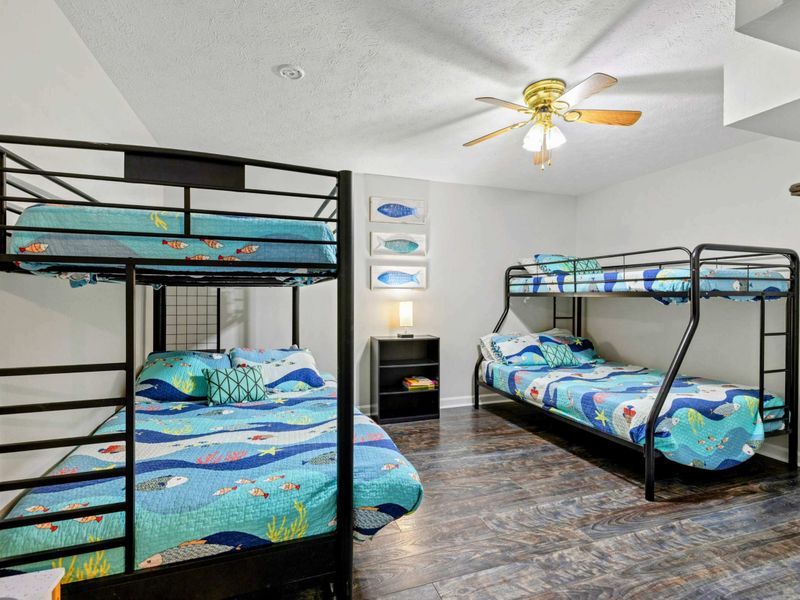 Bunk Room - Two full-over-full black metal bunk beds with colorful ocean-themed quilts, fish art, and a ceiling fan.