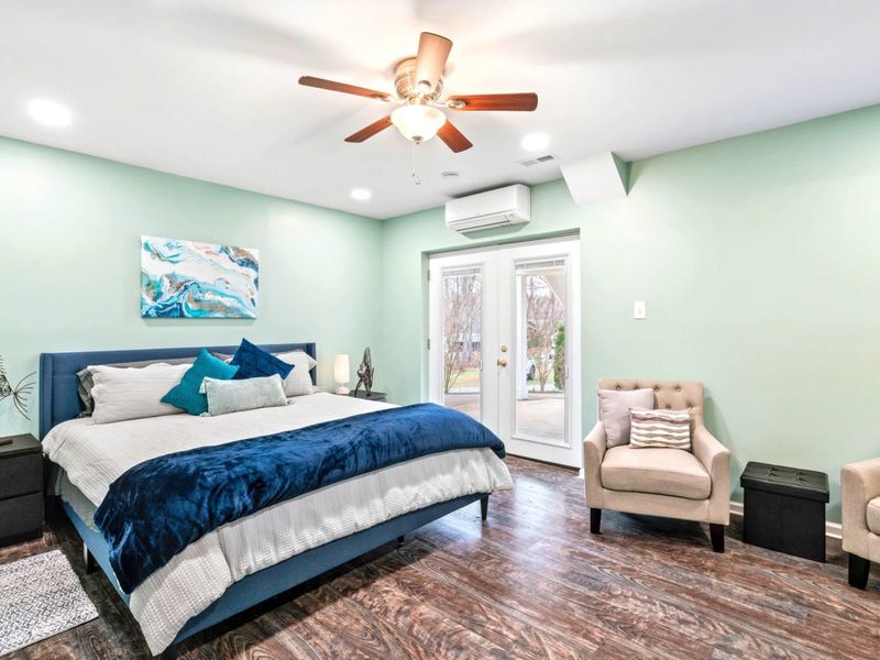 Primary Suite - Spacious king bedroom with mint green walls, navy upholstered bed, teal velvet throw, abstract art, and a seating area.