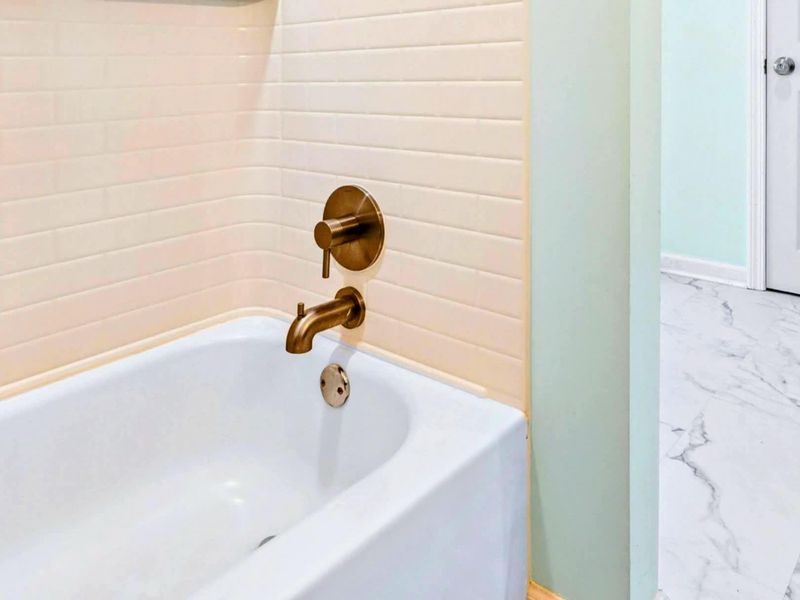 Primary Bathroom - Soaking tub with brushed brass fixtures and subway tile surround on marble-look flooring.