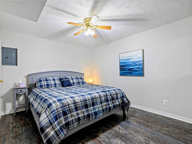 Bedroom - King bed with gray frame, navy plaid bedding, ocean wave canvas, and hardwood floors throughout.