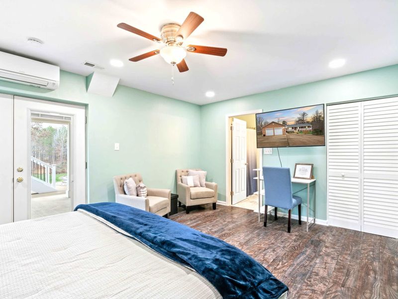 Primary Suite - Alternate angle showing the king bed, tufted accent chairs, wall-mounted TV, desk nook, and French doors to the yard.