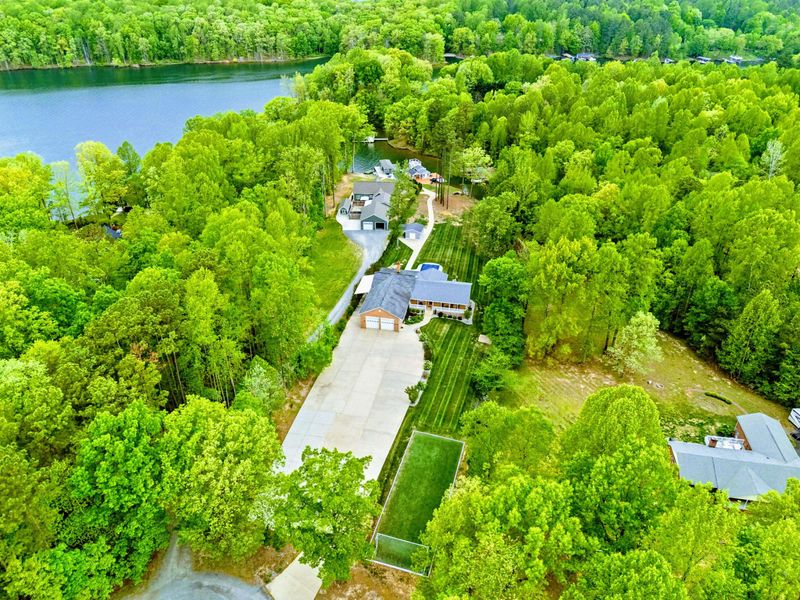 Aerial - Drone view of the property and long driveway surrounded by lush green trees with the lake visible beyond.