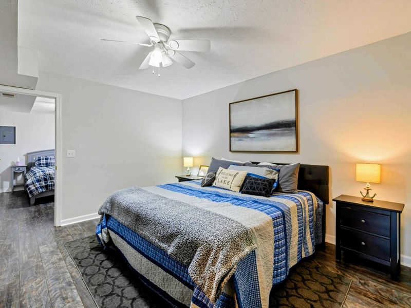 Bedroom - Queen bed with blue plaid bedding, a "Welcome to the Lake" pillow, landscape art, and dark nightstands.