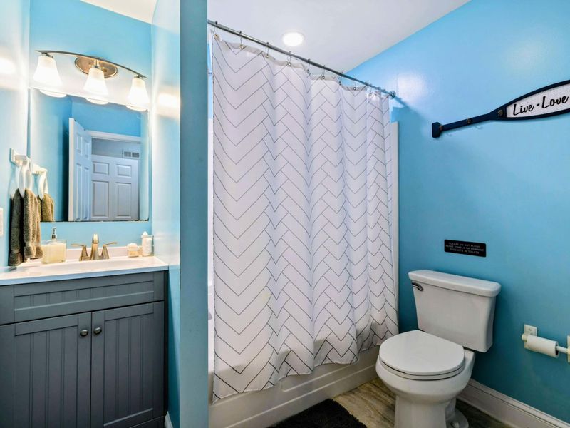 Bathroom - Sky-blue walls with a gray vanity, chevron shower curtain, and a "Live Love Lake" paddle sign on the wall.