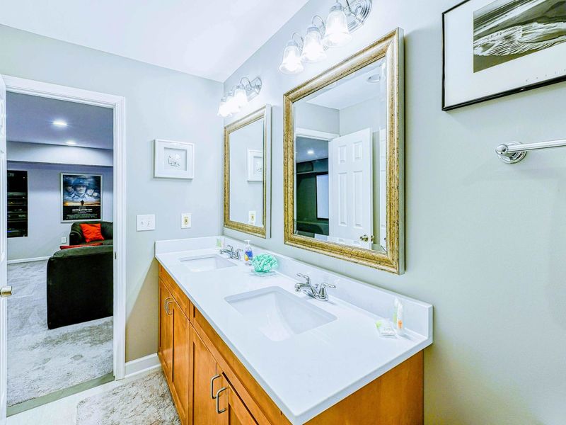 Lower Bathroom - Double vanity with gold-framed mirrors, white countertop, and doorway to the theater visible.