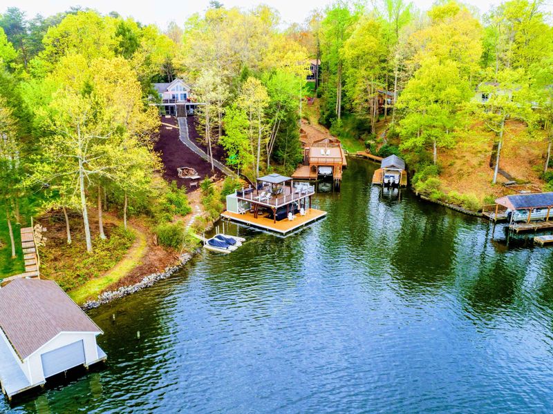 Aerial - Wider view of the property, dock, boathouse cove, and neighboring waterfront homes.