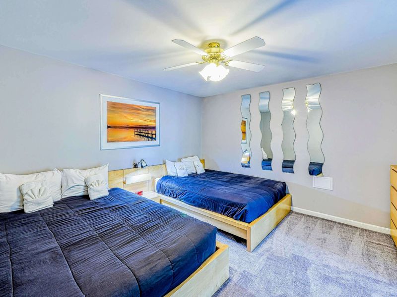 Bedroom 2 - Two queen platform beds with navy bedding, sunset dock art, decorative wave mirrors, and ceiling fan.