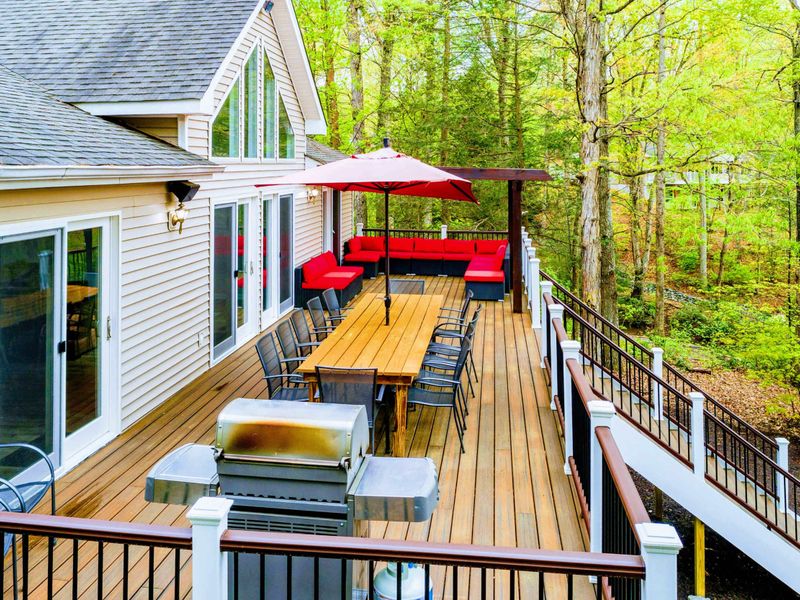 Deck - Elevated view of the dining table, red umbrella, pergola lounge, and gas grill under the tree canopy.