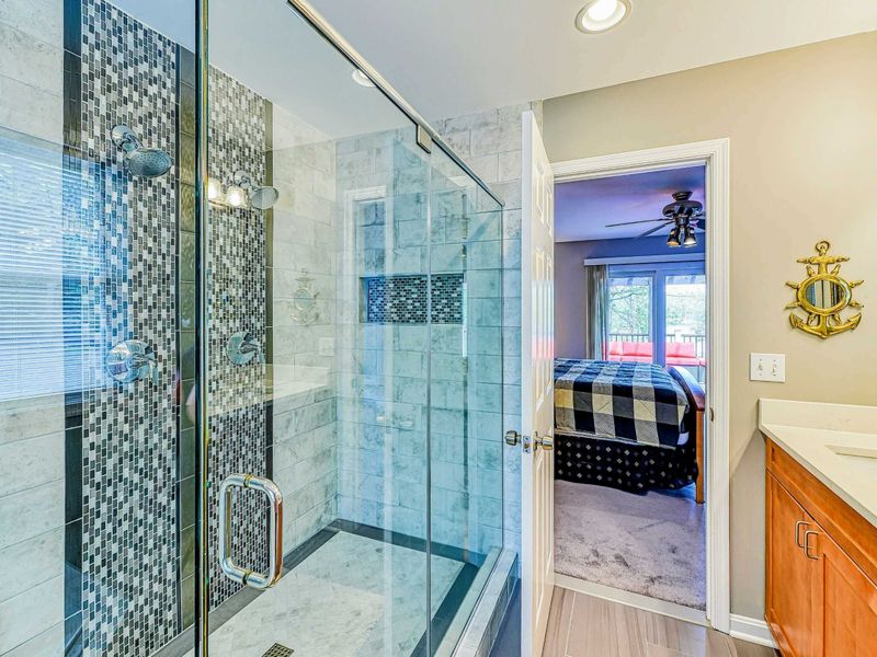 Primary Bathroom - Glass-enclosed walk-in shower with marble tile, blue mosaic accent stripe, and built-in niche.