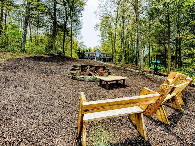 Fire Pit - Wood benches facing the lake with the home visible through the tall pines behind.