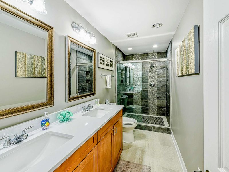 Lower Bathroom - Double vanity with dark slate walk-in shower, mosaic accents, and glass door.