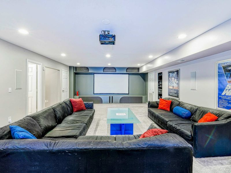 Home Theater - Projection screen with ceiling-mounted projector, two leather sectionals, surround sound, and movie posters.
