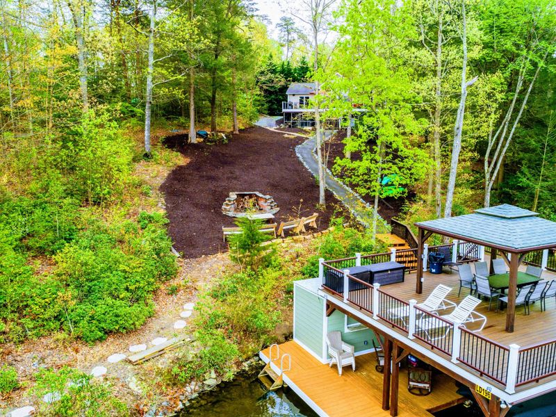 Aerial - Overhead view of the fire pit, Adirondack benches, sundeck gazebo, and dock on the waterfront.