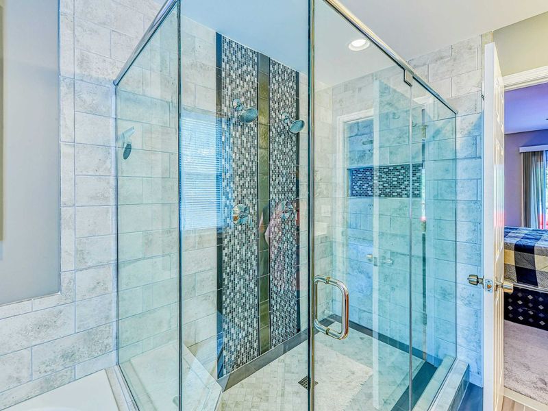 Primary Bathroom - Shower detail showing the marble tile walls, mosaic accent band, and frameless glass enclosure.