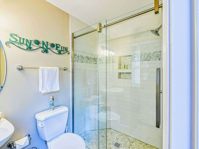 Bunk Room Bathroom - Glass walk-in shower with white subway tile, mosaic accent band, and coastal decor.