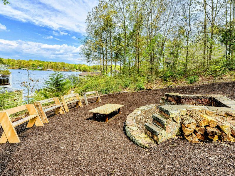 Fire Pit - Stone fire pit with wood benches overlooking the dock and lake through the trees.