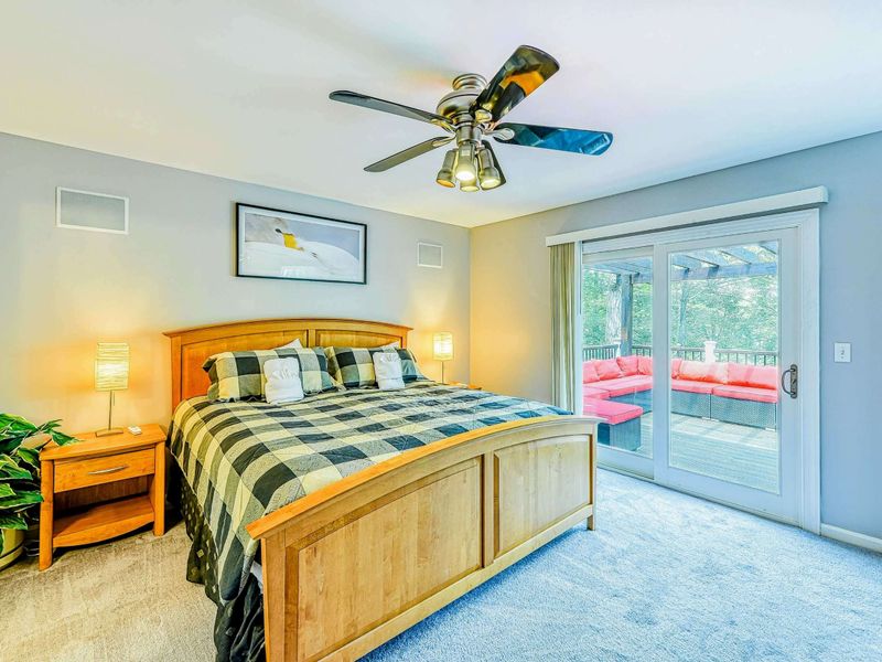 Primary Suite - King bed with maple sleigh frame, plaid bedding, ceiling fan, and sliding doors to the pergola deck.