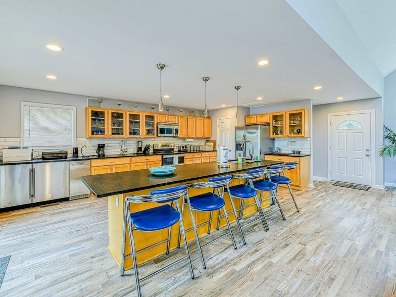 Kitchen - Large island with six blue bar stools, pendant lights, maple cabinets, and granite countertops.
