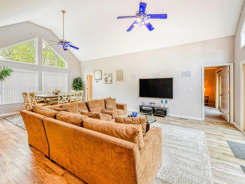 Living Room - Alternate angle showing the TV wall, dining nook, primary suite entry, and vaulted ceiling.