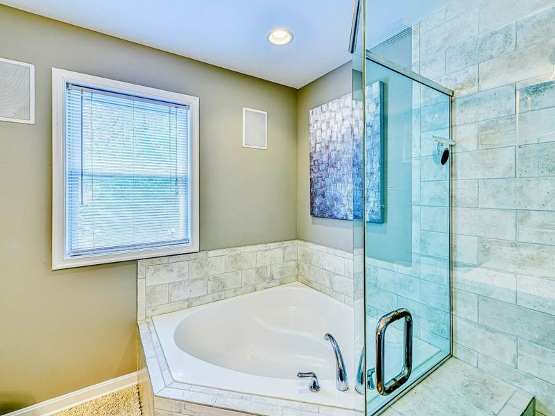 Primary Bathroom - Corner soaking tub with marble surround, window view, and glass shower adjacent.