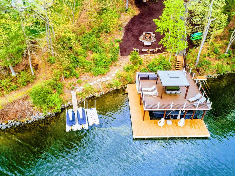 Aerial - Overhead view of the dock with paddleboards and floats in the water, fire pit, and gazebo sundeck.