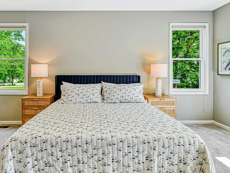 Primary Suite - Headboard detail with navy channel headboard, rattan nightstands, and marble-base lamps with garden views.