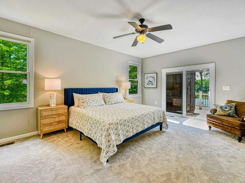 Primary Suite - King bed with navy channel headboard, floral bedding, rattan nightstands, ceiling fan, and sliding door to the sunroom.
