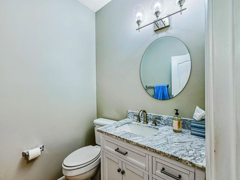 Powder Room - White vanity with marble countertop, oval mirror, and globe sconces on the main level.