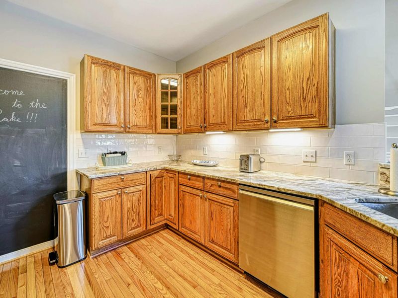 Kitchen - L-shaped counter with oak cabinets, dishwasher, chalkboard accent wall, and subway tile backsplash.
