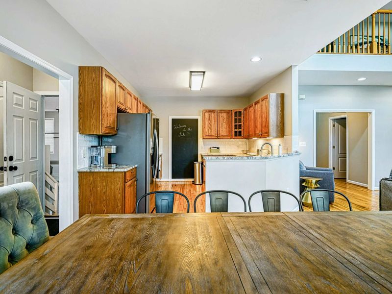 Kitchen - Dining table view into the kitchen with oak cabinets, chalkboard wall, granite peninsula, and loft above.