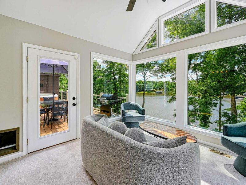 Sunroom - Alternate angle showing the curved sofa, door to the deck, teal accent chairs, and floor-to-ceiling lake views.