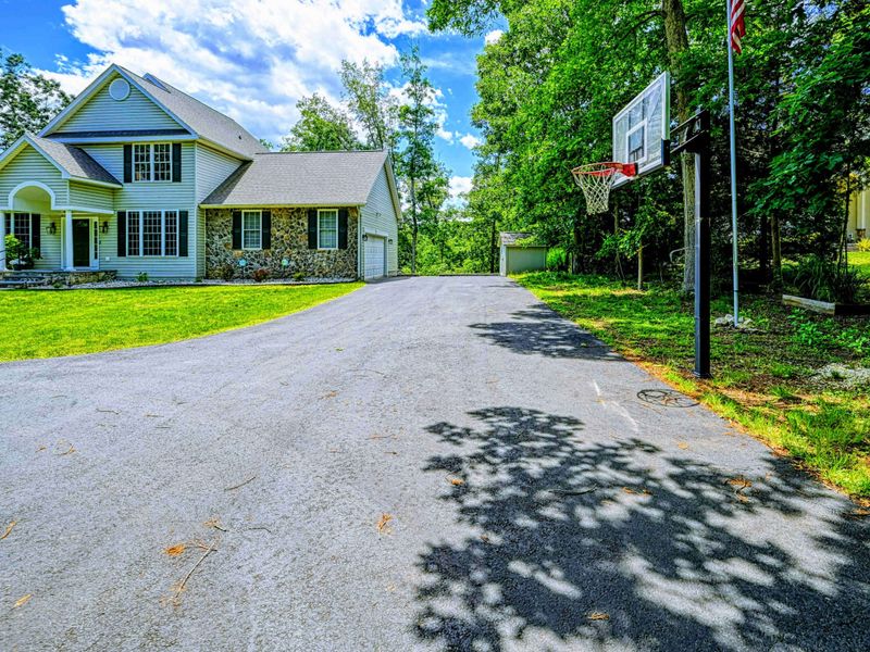 Driveway - Spacious paved driveway with basketball hoop, detached shed, and room for multiple cars.