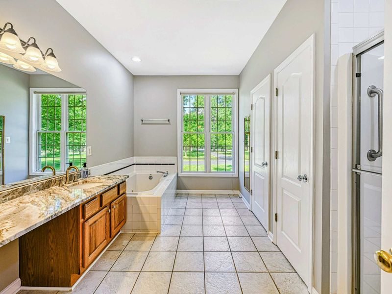 Primary Bathroom - Spacious en suite with granite double vanity, jetted soaking tub, glass-door shower, and yard-view windows.