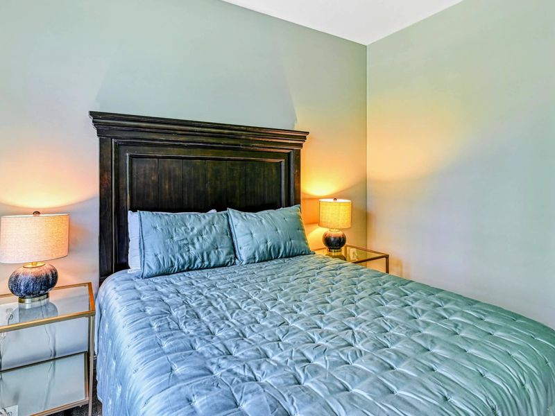 Bedroom 3 - King bed with dark wood panel headboard, teal pin-tuck bedding, and gold glass nightstands on the main level.