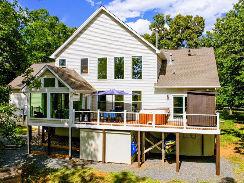 Exterior - Rear of the home showing the sunroom with A-frame windows, upper deck, hot tub area, and multiple levels.