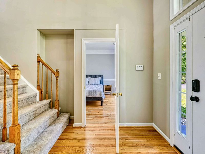 Foyer - Entry hall showing the staircase, oak railing, main-level bedroom entry, and front door sidelight.