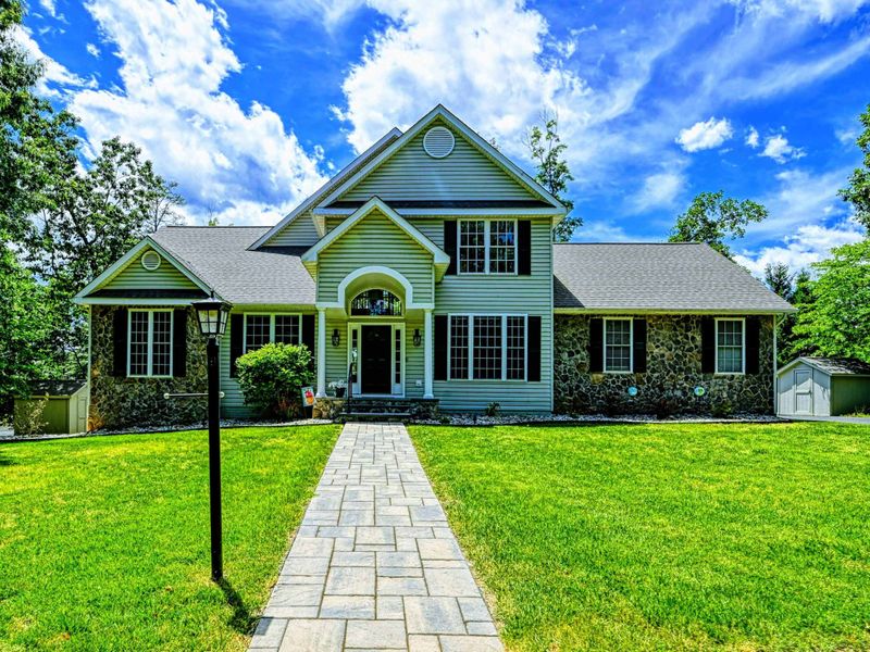 Exterior Front - Sage green colonial with stone accents, Palladian window, flagstone walkway, and manicured lawn.