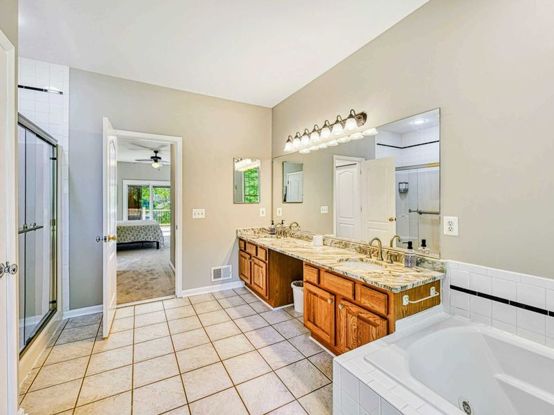 Primary Bathroom - Alternate showing the granite double vanity, glass shower door, soaking tub, and tile floor.