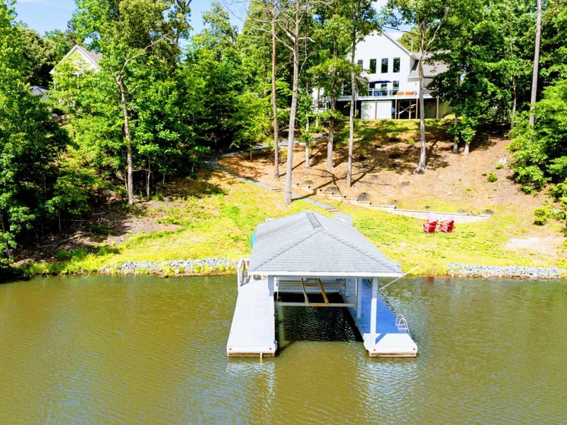 Aerial - Drone view from the lake showing the home on the wooded hillside with the dock, fire pit, and walkway below.